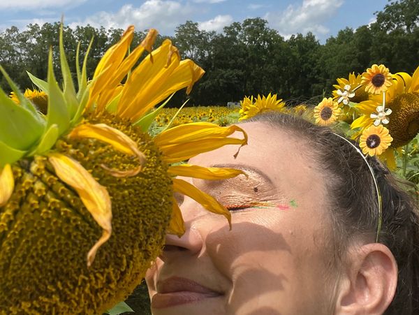 Woman enjoying a sunflower field with floral headband on a sunny day.