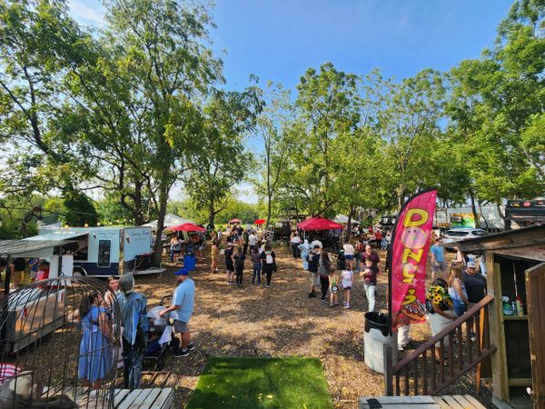 Outdoor market with people and food trucks under sunny skies.