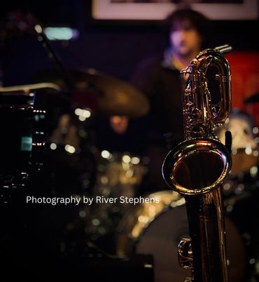 Close-up of a saxophone with a drummer blurred in the background.