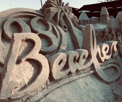 Intricate sand sculpture spelling out 'Beaches' with artistic waves and towers.