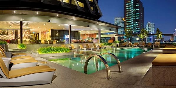 Luxurious outdoor swimming pool area at night with sun loungers and city skyline.