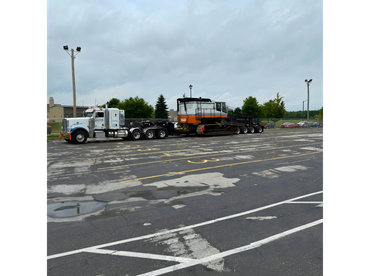 Truck transporting a large piece of construction equipment on a flatbed trailer.