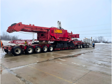 Heavy-duty red crane loaded on a multi-axle trailer during transport.