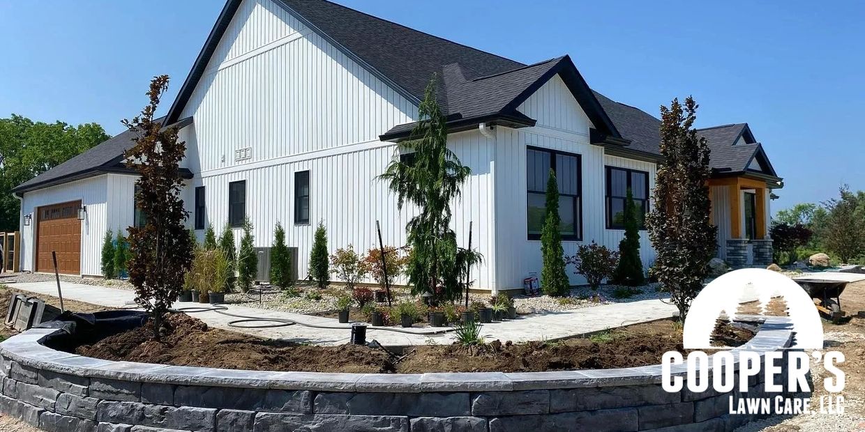 A modern white house with black roof and a stone retaining wall under landscaping.