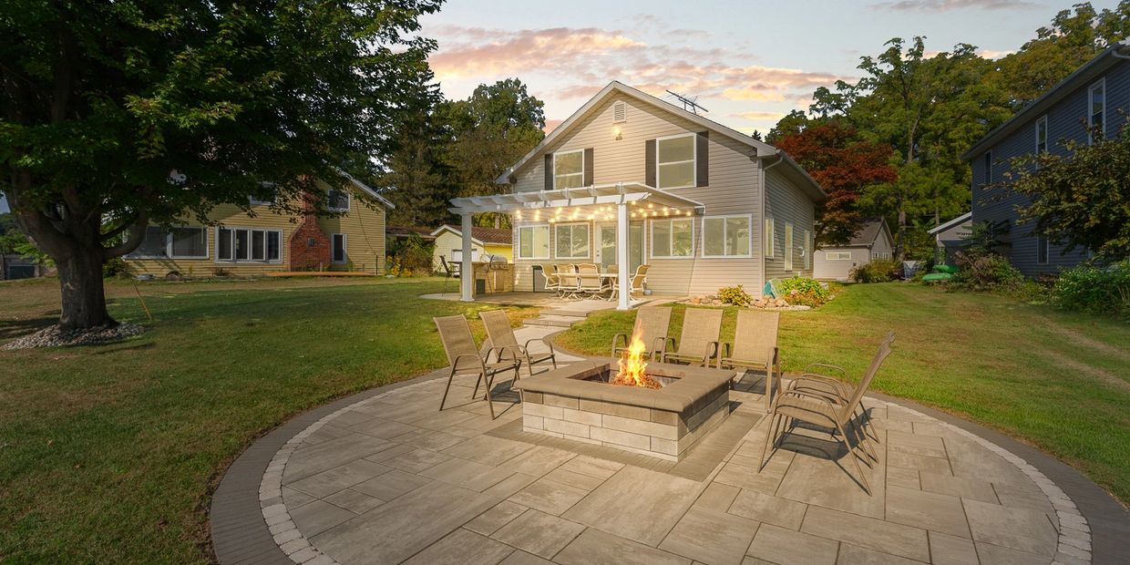 Backyard patio with fire pit and seating around a cozy house at sunset.