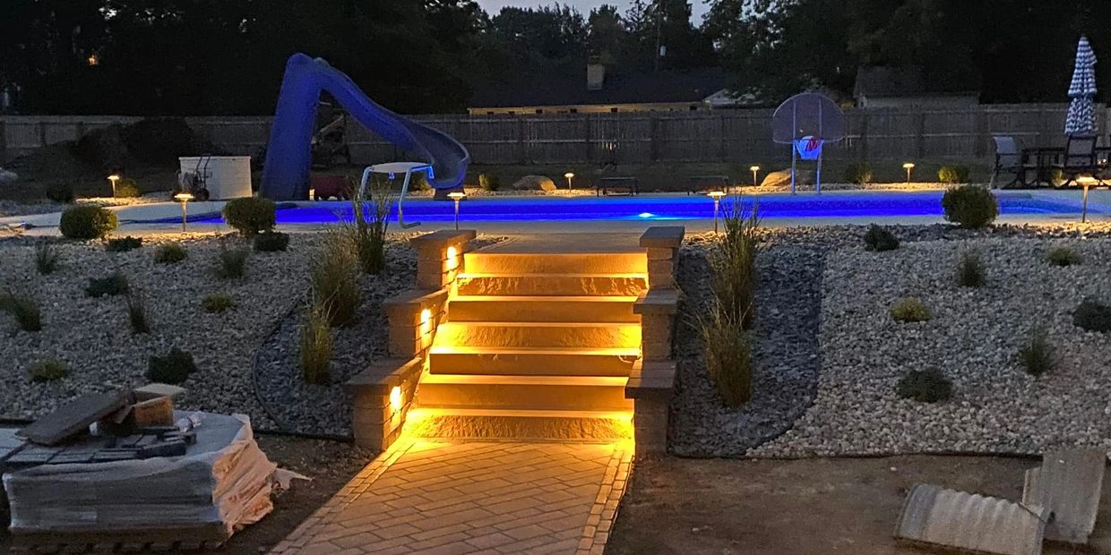 Illuminated stairs lead to a brightly lit swimming pool with a slide at night.