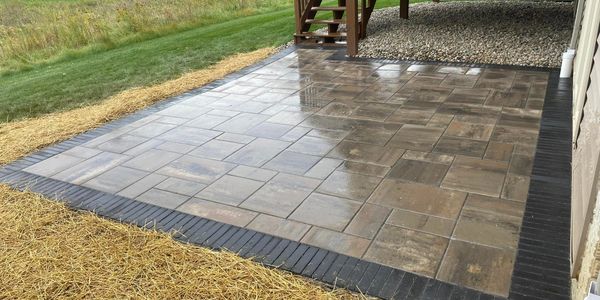 Newly installed wet stone patio with black brick border near a house.