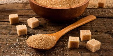 Brown sugar granules and cubes on a wooden surface with a wooden spoon.