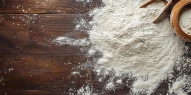 A pile of flour and wooden kitchen tools on a wooden surface.