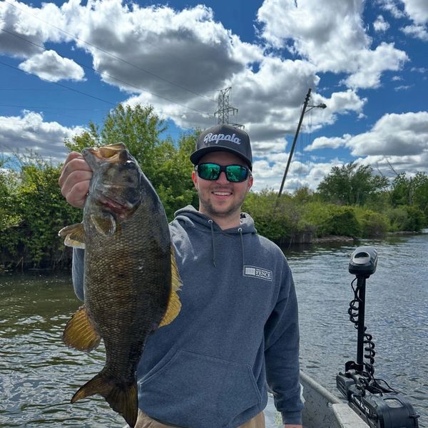Man holding a large fish on a boat under a cloudy sky.
