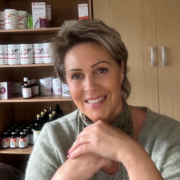 Smiling woman sitting with hands clasped, shelves of health supplements behind her.