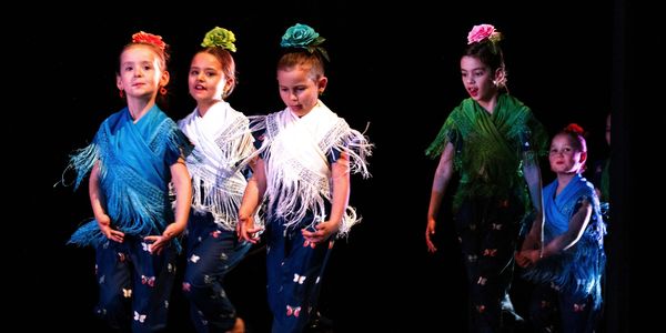 Children perform traditional dance wearing colorful shawls and flowers in their hair.