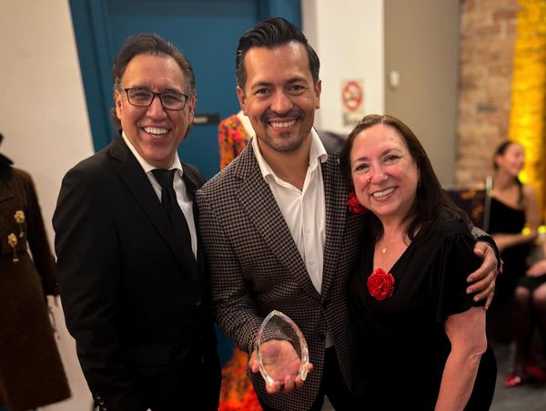 Three smiling people pose, one holding a clear award trophy.