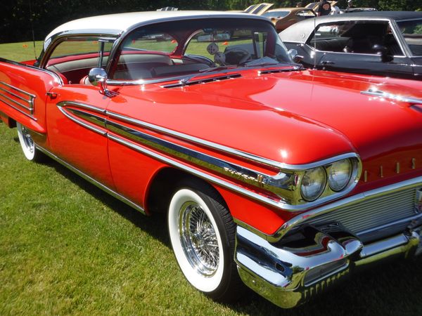 Classic red and white vintage car with chrome details parked on grass.