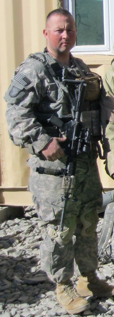 A soldier in full combat gear holding a rifle, standing outdoors.