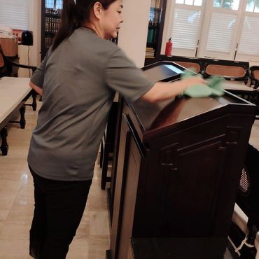 Woman cleaning wooden podium with cloth.