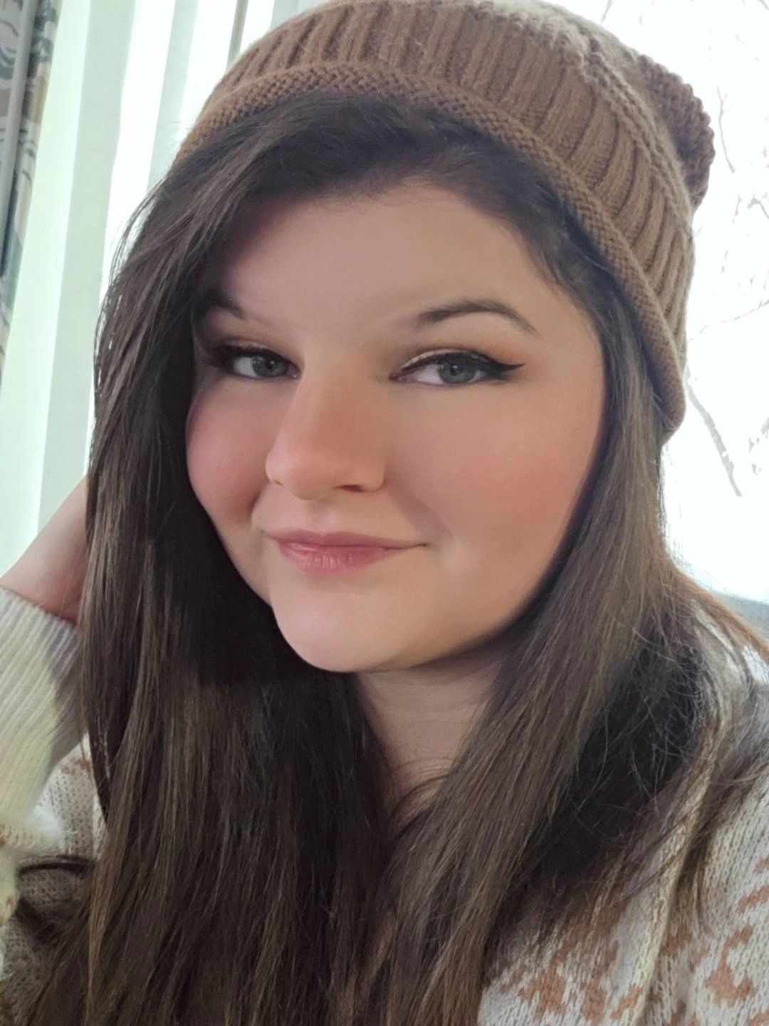 Woman with long brown hair wearing a brown knit hat and patterned sweater.