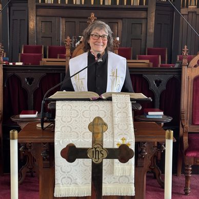 A smiling woman pastor stands behind a pulpit in a church sanctuary.