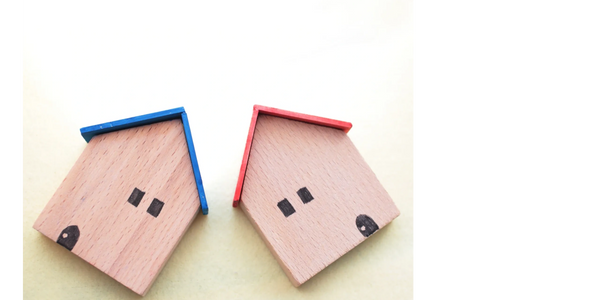 Two small wooden toy houses with blue and red roofs on a light background.