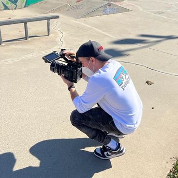A person crouching and filming with a professional camera at a skatepark.