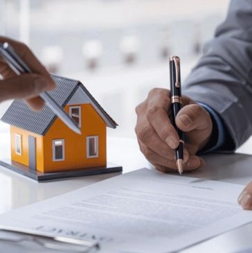 Person signing a real estate contract with a house model on the table.