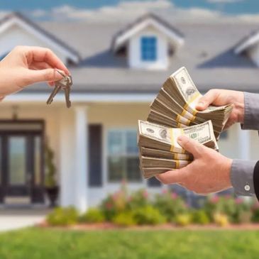 Hand exchanging house keys and cash in front of a home.