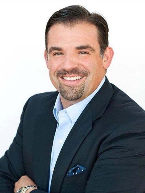Man with dark hair and facial hair smiling.