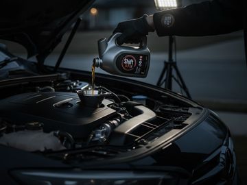 Person pouring motor oil into a car engine at night with a funnel.