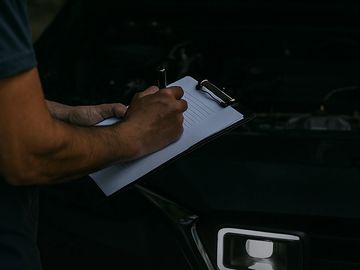 Person writing inspection notes during car pre-purchase check.