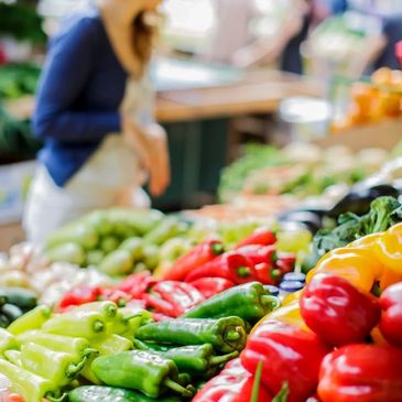 Colorful fresh peppers displayed at a market with a shopper in the background.