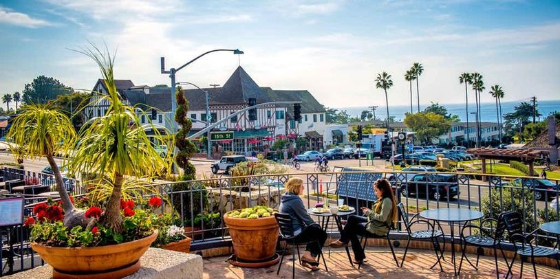 Two people enjoying a sunny outdoor cafe with ocean view.