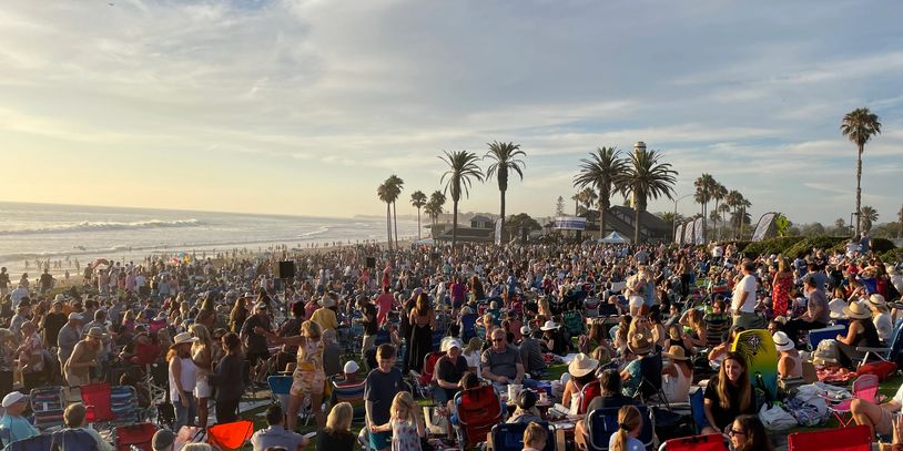Large crowd gathered on a beach at sunset.