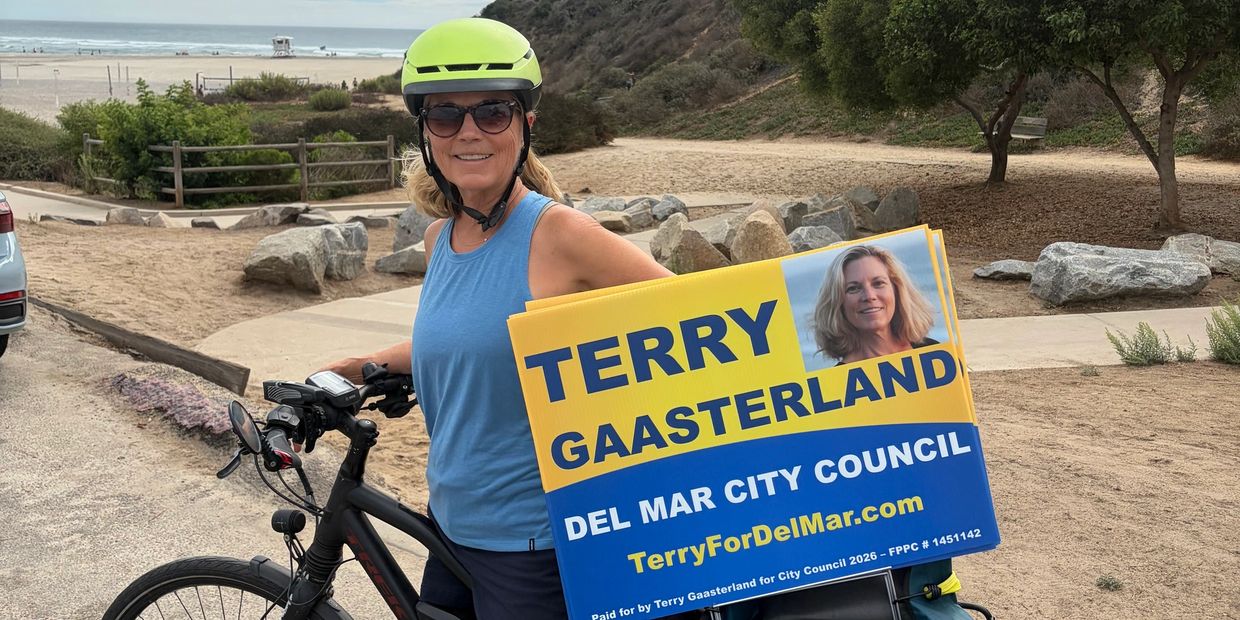 Woman on a bike holding a campaign sign for Terry Gaasterland.