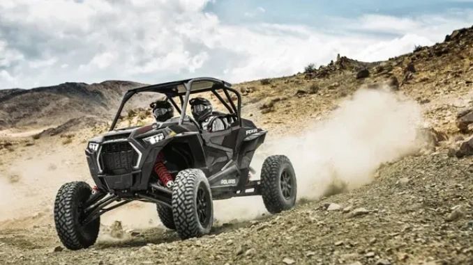 Two people riding a Polaris off-road vehicle on a dusty trail.