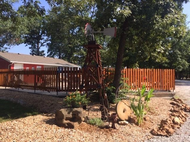A wooden windmill with a rooster on top in a garden bed.