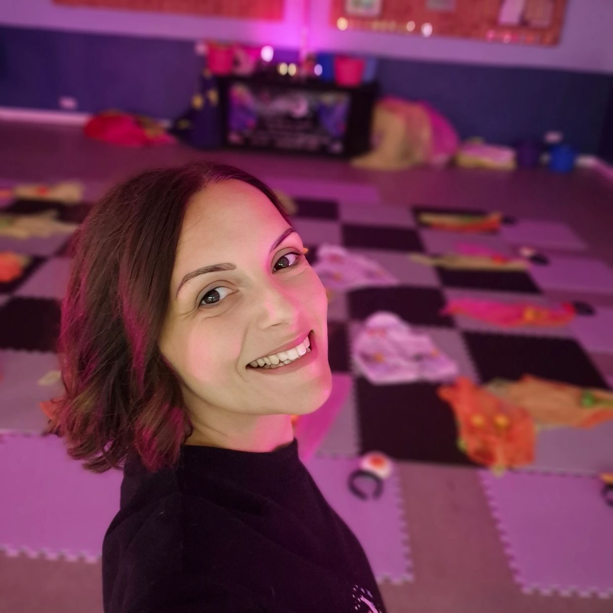 Smiling woman taking selfie indoors with purple lighting.