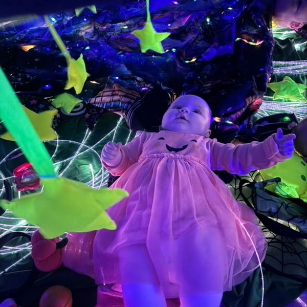 Baby in a pink dress surrounded by glowing stars and colorful lights.