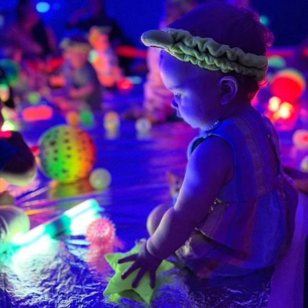 Baby playing with glowing toys in a dark room.