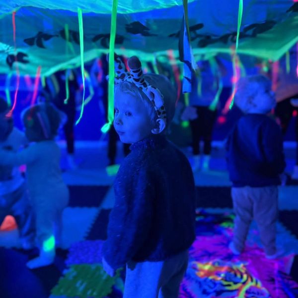 Children play under glowing neon ribbons in a dark, colorful room.