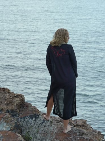 Person standing barefoot on a rocky shore looking at the sea.