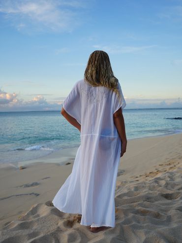 Person in white robe standing on the beach looking at the ocean.
