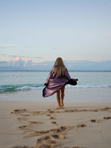 Woman walking toward the ocean at sunset.