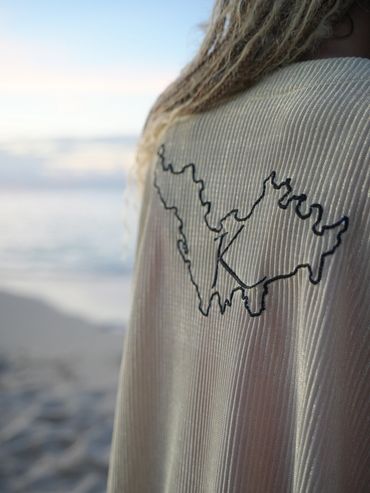 Close-up of a ribbed fabric with a black embroidered outline and long curly hair against a serene sky.
