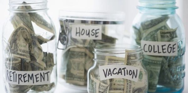 Four jars labeled for financial goals filled with cash.