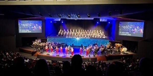 Orchestra and choir performing on stage with blue lighting and audience.