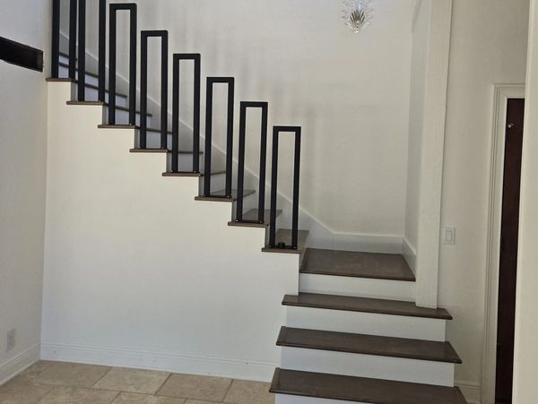 Modern staircase with dark wooden steps and minimalist black railings in a bright room.
