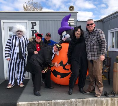 Group of adults in Halloween costumes posing outdoors with an inflatable pumpkin cat.