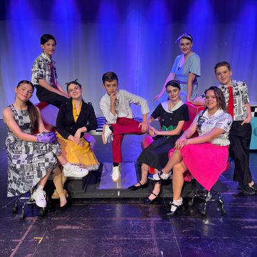 A group of young actors in 1950s-style costumes posing on stage.