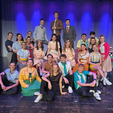 A group of young performers posing on stage in colorful costumes under blue lighting.