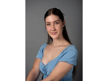 Young woman with long dark hair wearing a blue dress, smiling softly.